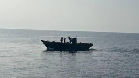 A wooden boat in the middle of the sea. Two people are seen standing on the boat