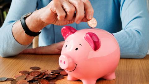 close up of someone's hands dropping coins into a piggy bank