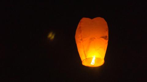 A burning sky lantern is floating off into the pitch black night sky.