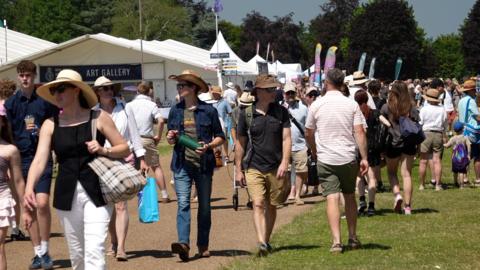 crowds milling at the Royal Norfolk Show wearing shorts and shirts and sunglasses with marquees in the background