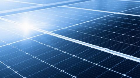 A stock image of solar panels, with the Sun shining on it. 
