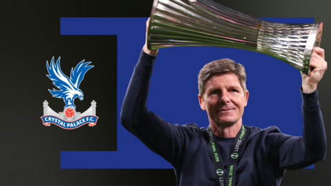 Oliver Glasner holds aloft the Conference League trophy, in front of a blue and black background and the Crystal Palace club badge
