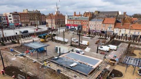 A drone shot of the Stockton Waterfront urban park shows construction work is well underway. Scaffolding surrounds a large structure and lots of vans and construction equipment are parked nearby.