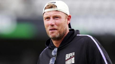 A man with short light brown hair and a beard is wearing a white baseball cap backwards and a dark blue jacket with 'Northern Super Chargers' written on it.