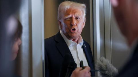 President Donald Trump speaks into two microphones in the doorway of Air Force One's press room