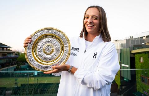 iga swiatek smiling while holding the wimbledon ladies singles trophy on a balcony at wimbledon