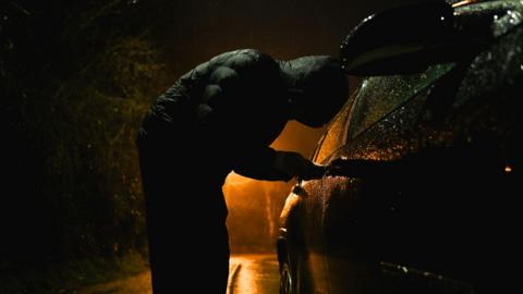 Man with hood trying to break into car.