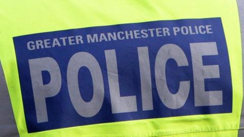 Close up image of a Police vest. Luminous yellow in colour with a blue box in the middle - within which 'Greater Manchester Police' is written in grey text.