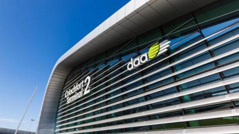 Image of the outside of Terminal 2 at Dublin Airport, with 'DAA' logo. The sky is blue and clear. 
