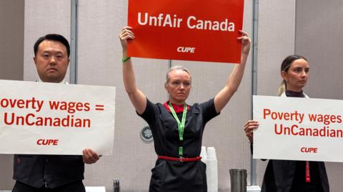 Union activists hold placards, as they interrupt a press conference by Air Canada executives, ahead of a potential strike by Air Canada flight attendants, at a hotel in Toronto, Canada, on 14 August 2025.