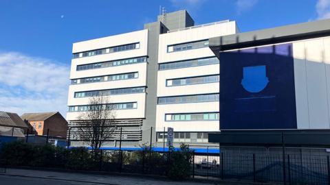 View of the seven-storey Derek Crothall Building in Hull with white walls and tinted windows and a blue patch where the school badge used to be