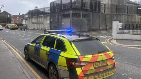 A yellow and blue police car parked outside Strabane police station
