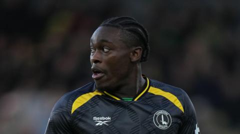 Tanto Olaofe looking to his right, playing for Charlton in a dark grey/black away kit with a yellow trim