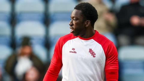 Ephraim Yeboah wearing a long sleeve training top ahead of a Bristol City match with blue seats blurred in the background