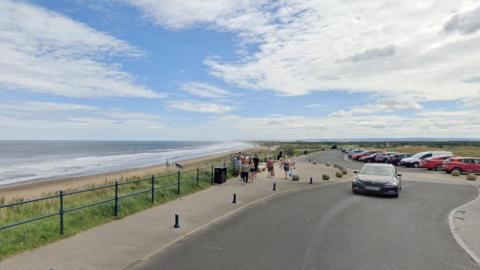 A busy beach car park. The beach can be seen to the left.