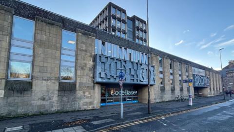 A general view of the rear of Argyle House. The building is low and is made of light stone with dark motifs above the door and windos to the left side.