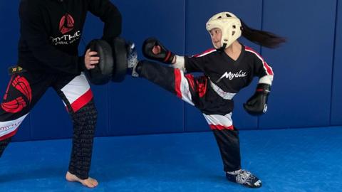 Six-year-old Ivanna performs a high kick during pad work training with her father