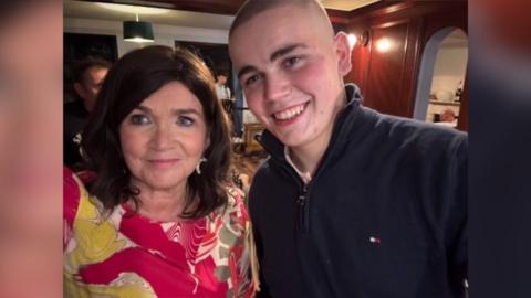 A woman in a brightly-coloured dress and dark hair is pictured with a man in a dark coloured top