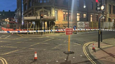 Blue police tape stretched across Great George Street in Leeds with a red and white footpath closed sign