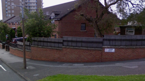 A GV of a road called Thorn Drive with a street sign on a red brick wall and some houses and trees in the background 