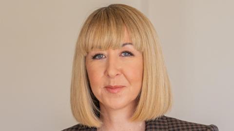 Michelle Niziol looks at the camera with a subtle smile on her face in a professional-looking headshot. She has neat, shoulder-length blonde hair and is wearing a chequered blazer. 