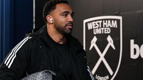 Callum Wilson walks past a West Ham badge on the wall