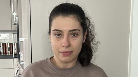 Emily Martins in her flat. She wears a taupe jumper.