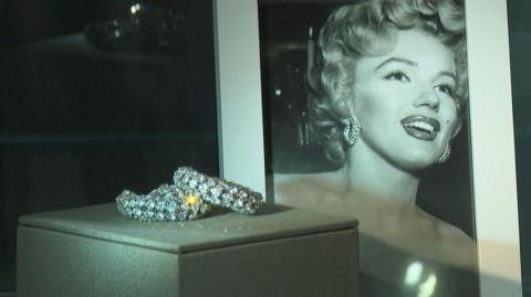 Sparkling earrings sit in a glass case in front of a portrait of Marilyn Monroe