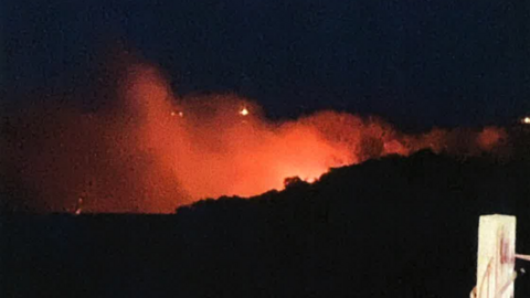 Red glow of flames in a night sky against a dark hillside.