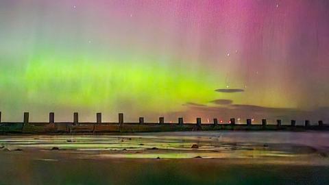 A dramatic glowing purple and green sky can be seen at night time as the northern lights illuminate the starry sky over a groin on the beach in Aberdeen with the tide out, uploaded to Weather Watchers on 12 September