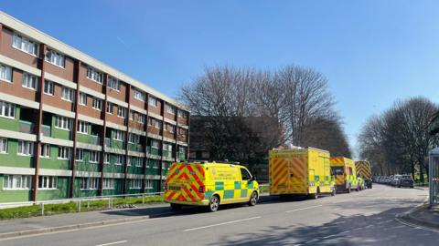A row of ambulances parked in the road outside a four-storey block of flats