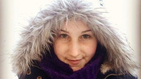 A young woman in her late 20s wearing a fluffy coat and looking into the camera.