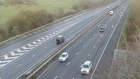 A traffic camera image of the A1(M) in Hertfordshire. Cars can be seen heading along the motorway with their headlights on during the early morning commute. 