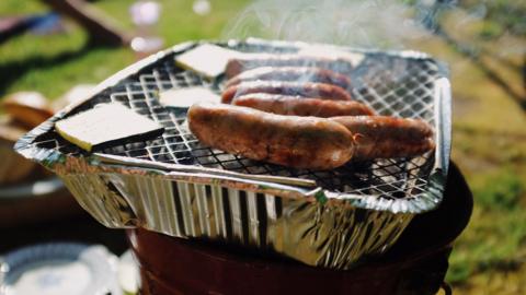 Sausages cooking on a disposable barbecue