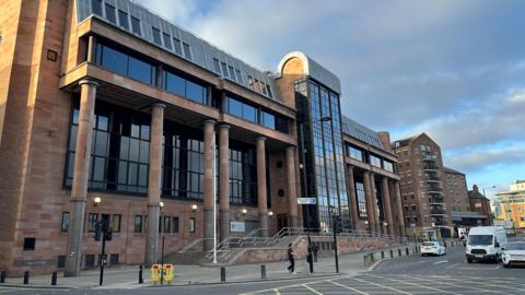 The imposing Newcastle Crown Court building made from smooth red stone with large columns and long dark windows.