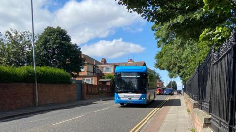 Blue Stagecoach bus driving along road on sunny day with trees on both sides. 