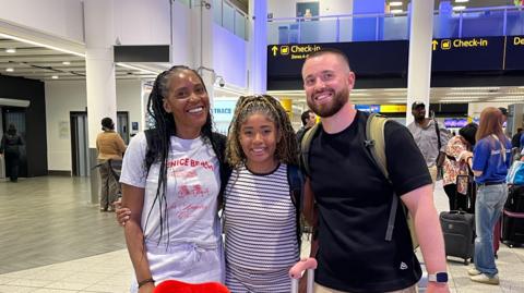 A family is standing together at the airport. They are all smiling.