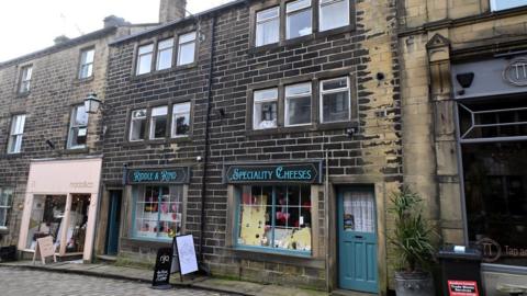 A row of old cottages, including a specialty cheese shop, on a cobbled street.