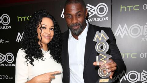 Kanya King and Idris Elba standing together, she's pointing at him and he's holding a Mobo trophy