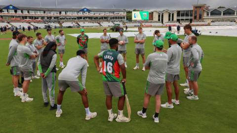 Leicestershire players in a huddle with covers on the pitch behind