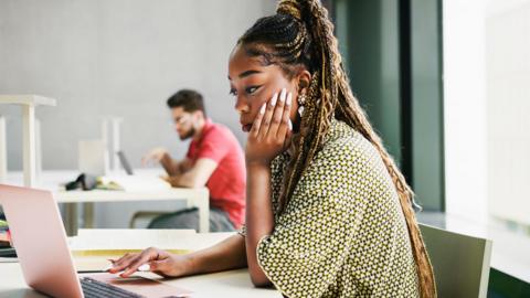 A young woman working from a laptop in an modern office.