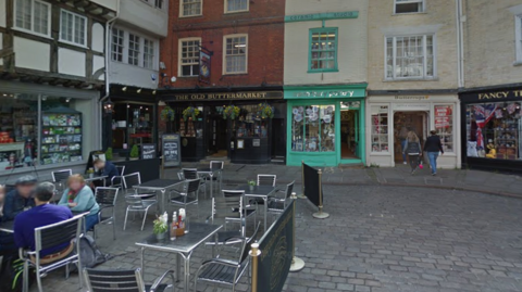 A cobblestone square with shops and outdoor seating.