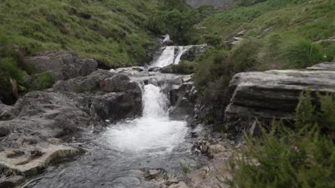 A national park's beauty spot shows a waterfall and rocks surrounded by a pool.