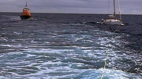 The yacht being towed in open water with the lifeboat standing off