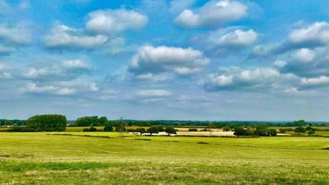 Green and yellow fields stretch to the horizon with blue sky and clouds above