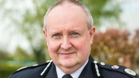 Cheshire Police Chief Constable Mark Roberts in his police uniform. He is a middle-aged man with receding light grey hair and blue eyes. There are trees in the background.