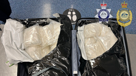 An opened suitcase with clear bags of white powder in both ends. Australian Border Force and Australian Federal Police crests are in the top right corner