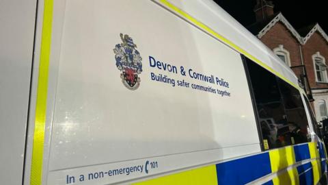 The photo shows a close-up of the side of a Devon and Cornwall police van with the words 'building safer communities together' printed on the side.
