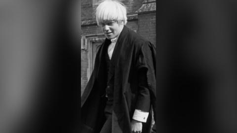 A black and white photo of a young man wearing school robes 