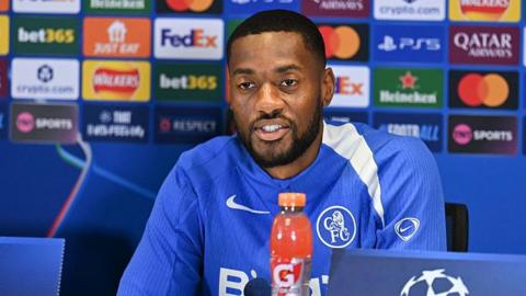 Tosin Adarabioyo wearing a Chelsea training top and speaking at a news conference